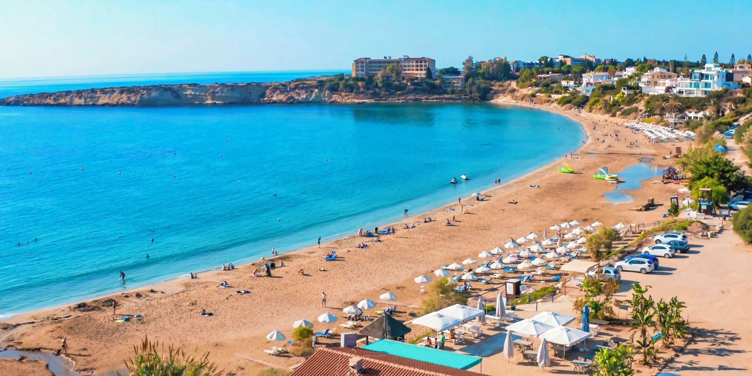Coral Bay Beach near Paphos in Cyprus, showing its golden sandy shoreline, clear turquoise Mediterranean waters and limestone coastline.